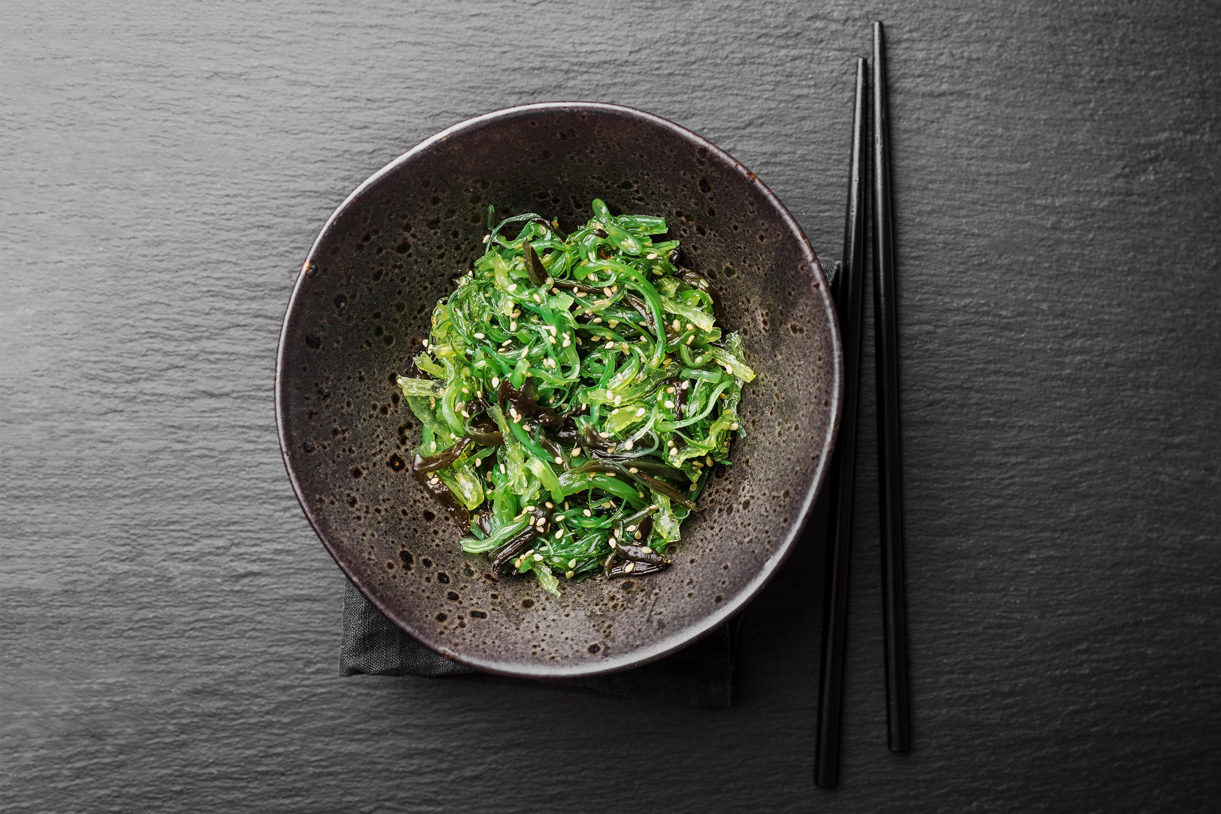 Tasty appetizing seaweed salad on dark plate on slate background.