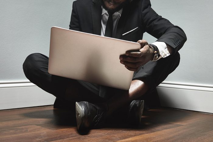 business man sitting on the floor in the corner with laptop