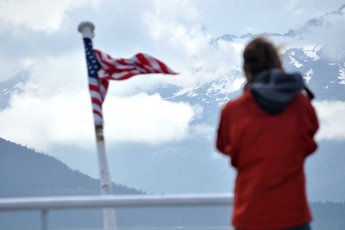 a figure braves the wind to gaze upon an american flag with mountains in the background
