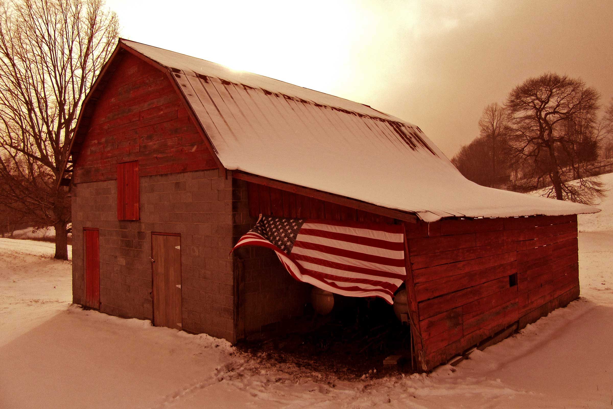 a large american flag waves on the side of a red barn in a snowy landscape in Cool Ridge, West Virginia