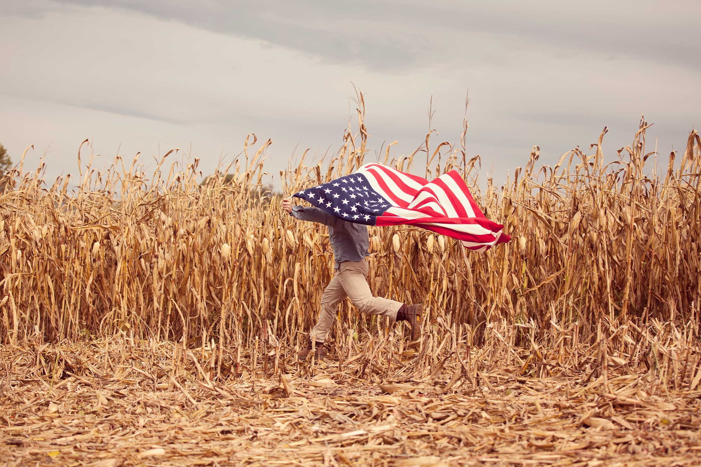 a retired Marine runs across his family’s cornfield in Harrisonburg, Virginia holding an american flag above his head