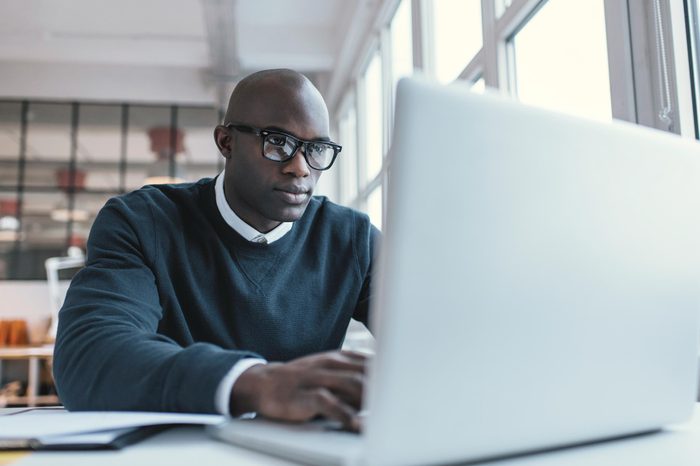 Young businessman working on his laptop in office. Young african executive sitting at his desk surfing internet on laptop computer.