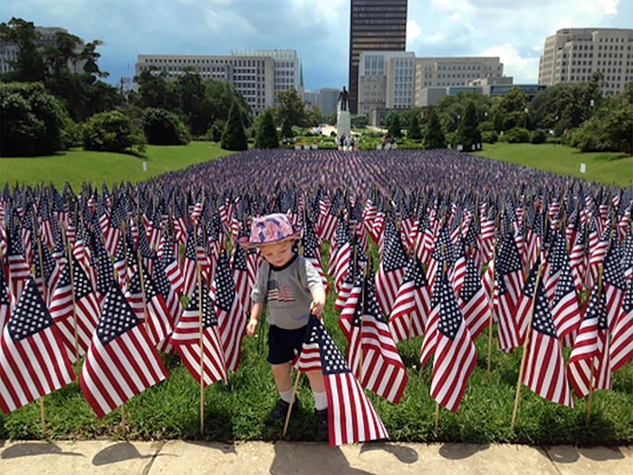 a young boy stands among a field of american flags and reaches to adjust one that is leaning; Zachary, Louisiana