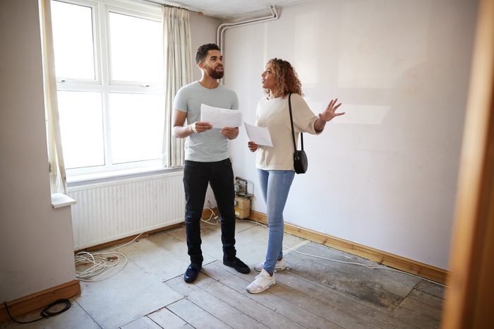 Couple Buying House For First Time Looking At House Survey In Room To Be Renovated