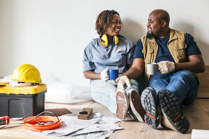 couple taking a break from renovations. smiling at eachother with coffee mugs.