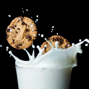 two chocolate chip cookies splashing into a glass of milk. black background.