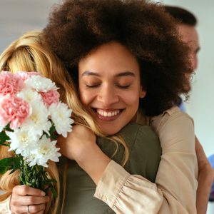 Shot of a woman hugging a friend and holding flowers.