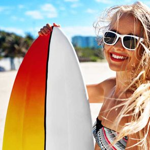 blonde woman smiling with surfboard on summer beach