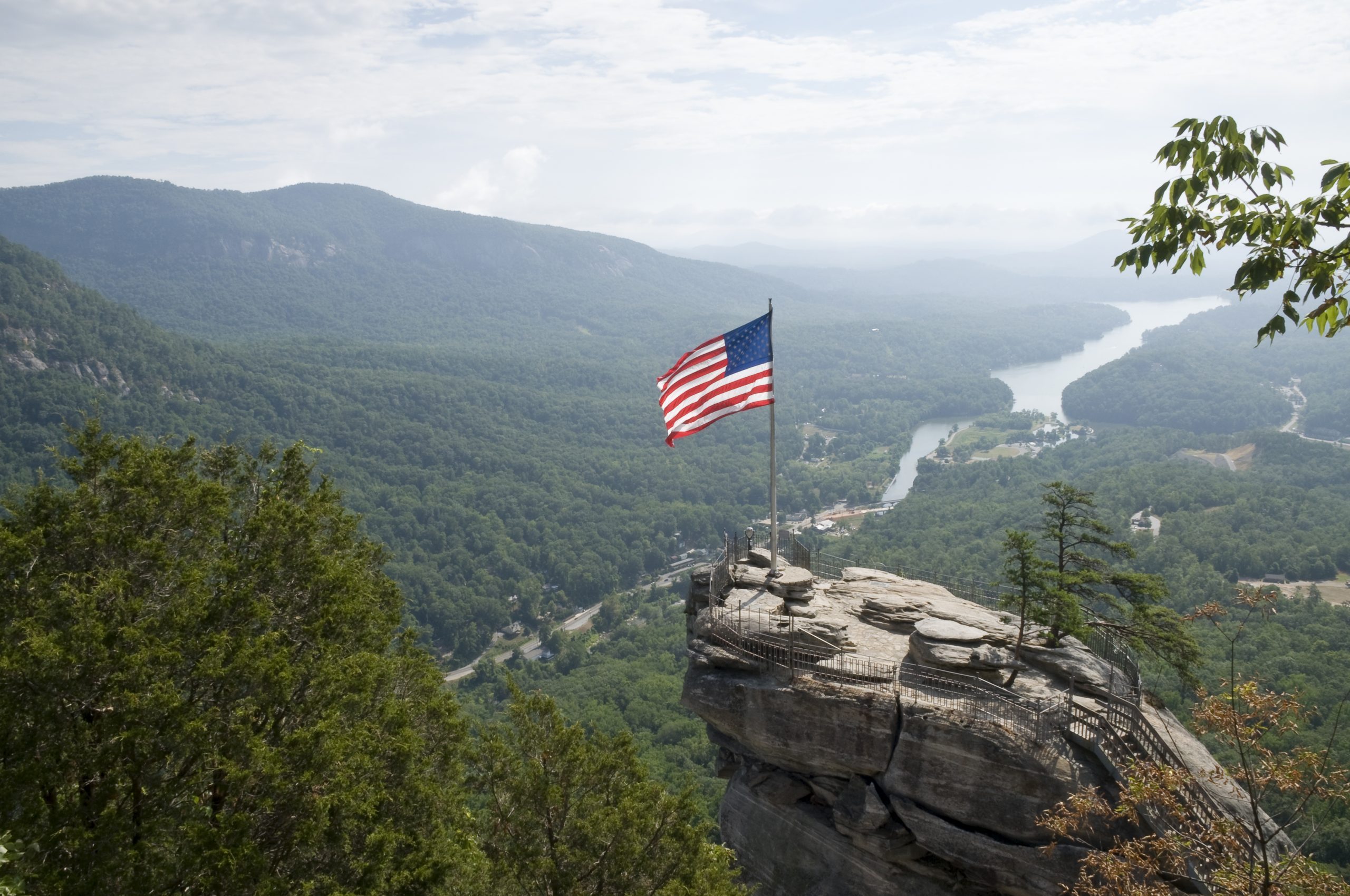 aerial shot of the top of Chimney Rock, North Carolina, with a waving American flag, and Lake Lure in the background