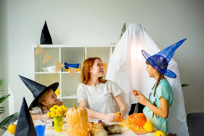 girls in halloween cosutmes look at kid dressed as a ghost in a white sheet