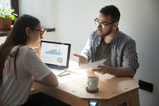 Two millennial coworkers having argument and business dispute in office. Businessman showing businesswoman paper document with working problems