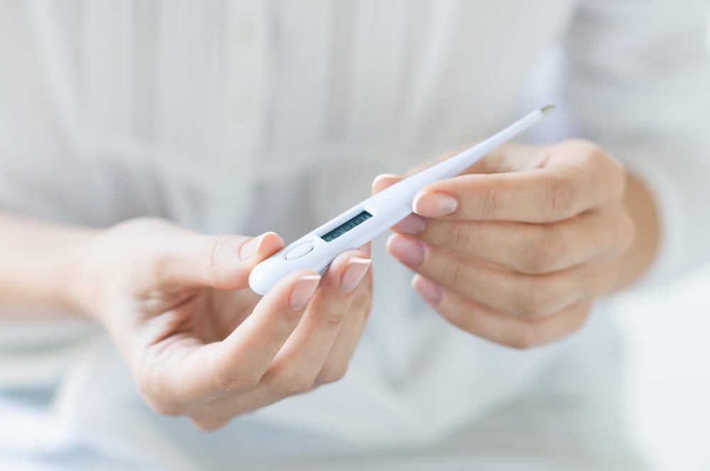 Closeup shot of a woman looking at thermometer. Female hands holding a digital thermometer. Girl measures the temperature. Shallow depth of field with focus on thermometer.