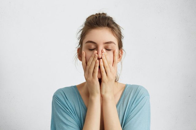 Headshot of young beautiful student female closing her eyes holding hands on chin being tired after hard work trying to relax for a minute and to gather her thoughts. Tiredness, feelings concept