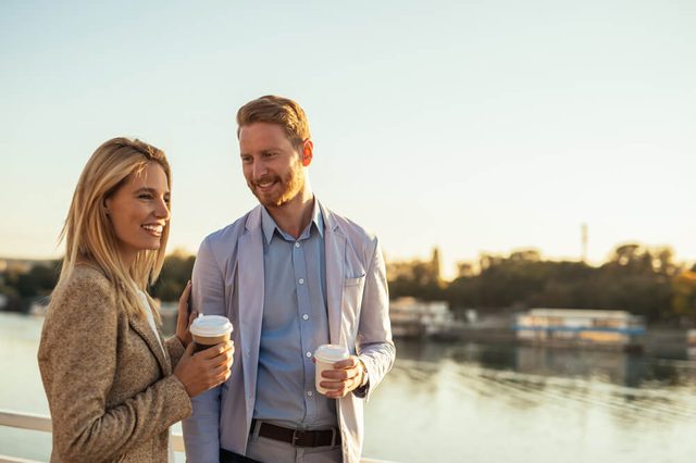 Friends taking a break from work walking by the river and drinking coffee.