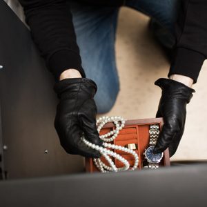 theft, burglary and people concept - thief stealing valuables from safe at crime scene