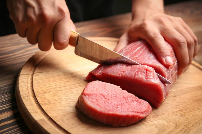 Chef cutting fresh raw meat on wooden board