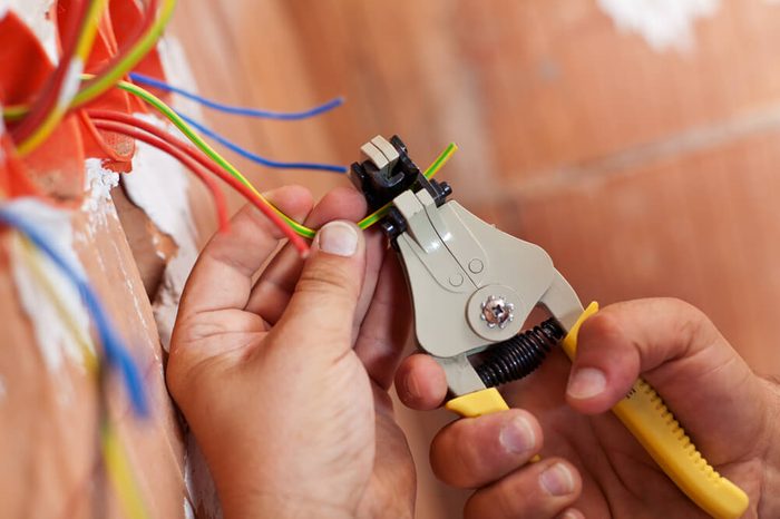 Electrician peeling off insulation from wires - closeup on hands and pliers