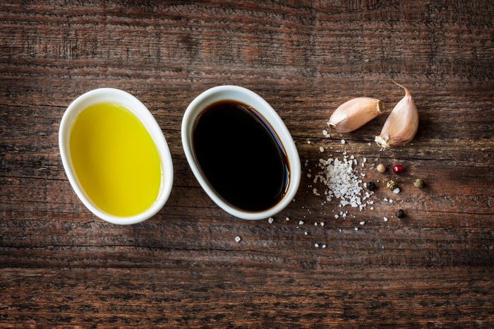 Vinaigrette or french dressing recipe ingredients on vintage wood background. Olive oil, balsamic vinegar, garlic, salt and pepper from above.