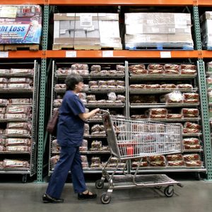 A shopper walks past shelves of bread at a Seattle Costco store . Costco Wholesale Corp. reported a 32 percent jump in its fiscal third-quarter profit Thursday, topping Wall Street expectations, as cash-squeezed customers flocked to its warehouse clubs in search of bargains on food and toiletries