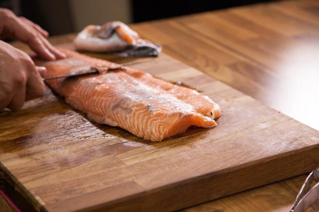 Close up of chef cleaning salmon skin with a knife for fillets.