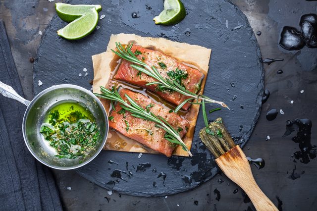 Pieces of raw salmon oiled marinade with spices, lemon, spices and olive oil with brush on slate stone on a dark metallic background. View from above. Preparation for cooking fish food. Salmon steak.