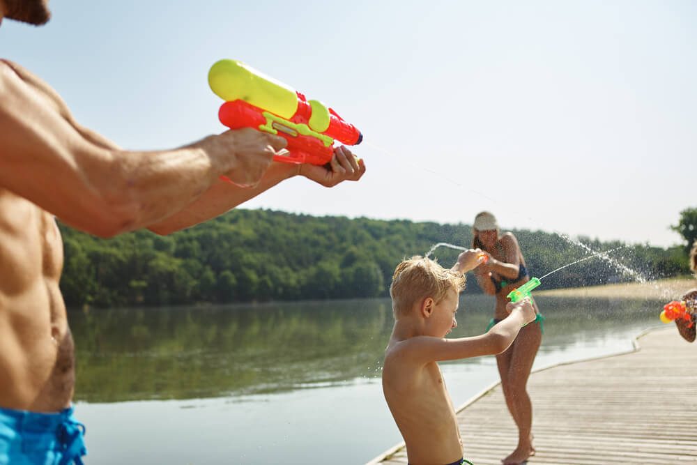 Family at a lake spraying water to each other with a squirt gun and having fun in summer