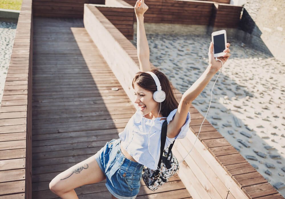 Emotional young woman with headphones listening music outdoors, summer girl portrait