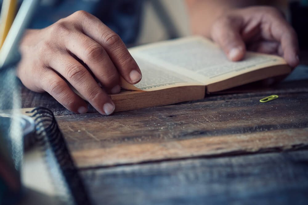 side view of man reading the bible in the darkness over wooden table.vintage effected photo.