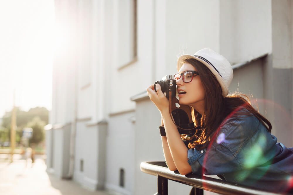 Summer closeup street portrait of young smiling beautiful and happy woman photographer posing with camera, wearing a hat