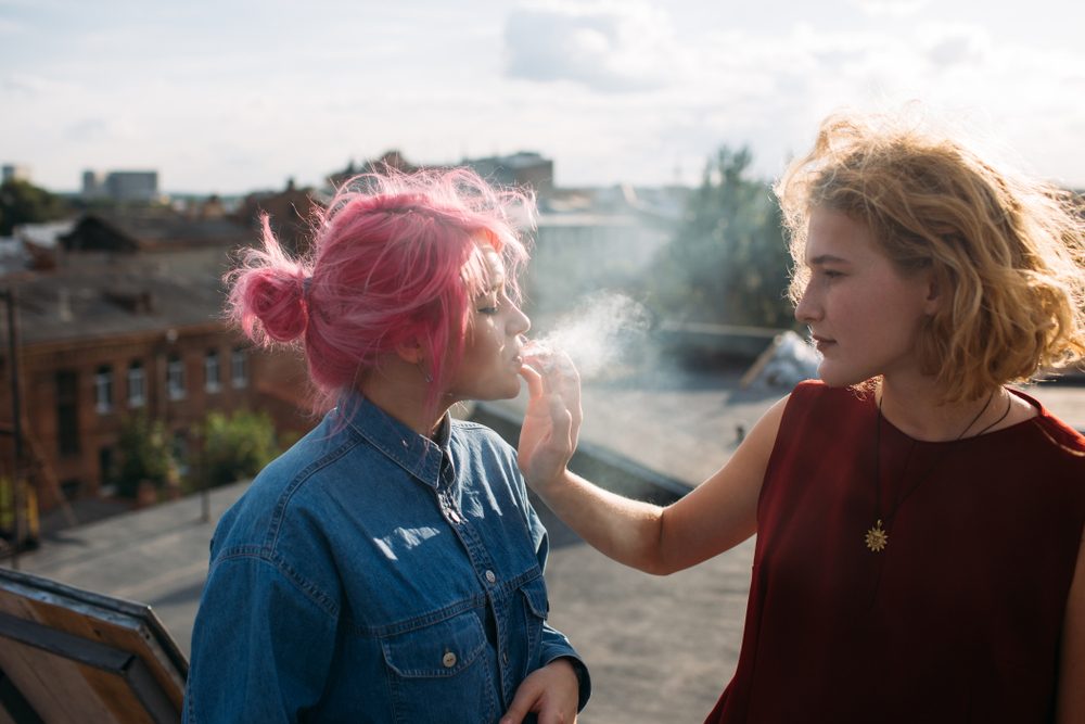 Bad influence. Girl smoking a cigarette from her friend's hand. Street teenage lifestyle. Dangers of bad associations