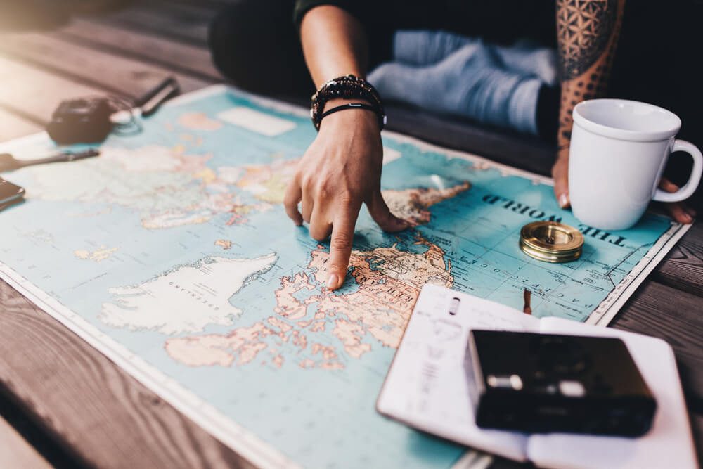 Tourist planning vacation with the help of world map with other travel accessories around. Young woman pointing at North America on the world map.