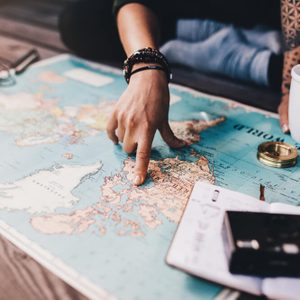 Tourist planning vacation with the help of world map with other travel accessories around. Young woman pointing at North America on the world map.