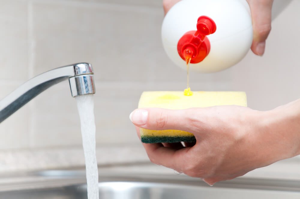 woman hand holding yellow sponge and pouring cleaning liquid on it