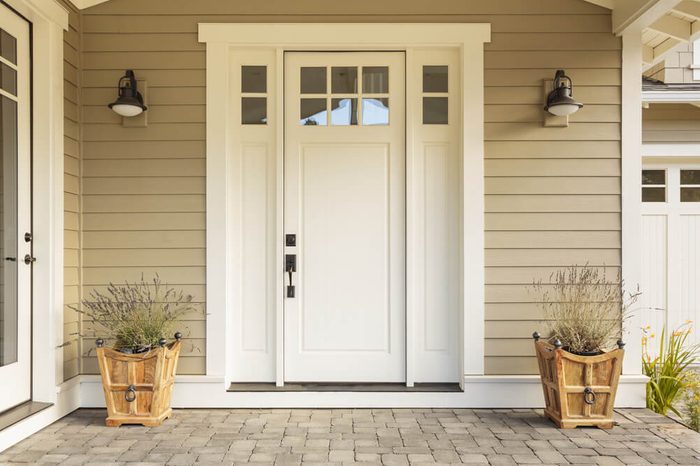 White front door with small square decorative windows and flower pots