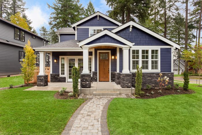 Beautiful exterior of newly built luxury home. Yard with green grass and walkway lead to ornately designed covered porch and front entrance. 