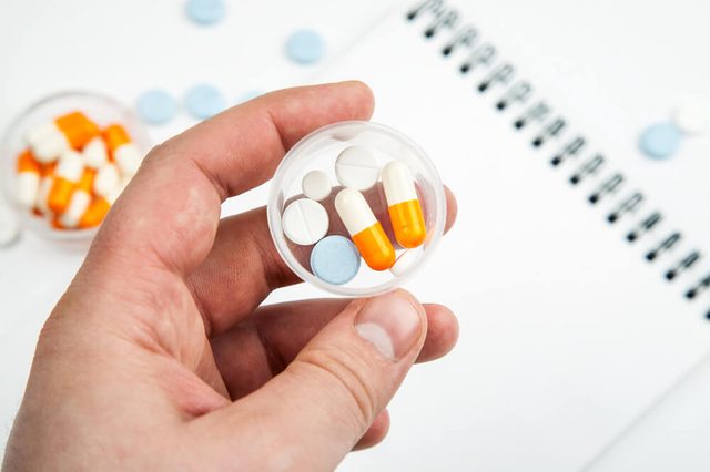 Hand holds plastic cup with dose of different medications