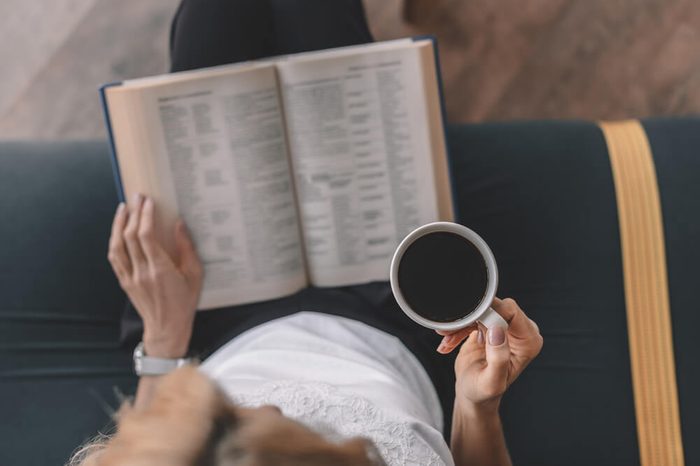 overhead view of woman reading book and drinking coffee in cafe