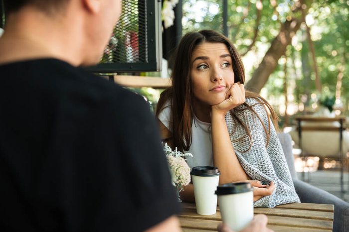 Tired bored girl sitting and drinking coffee with her boyfriend at a cafe outdoors and looking away