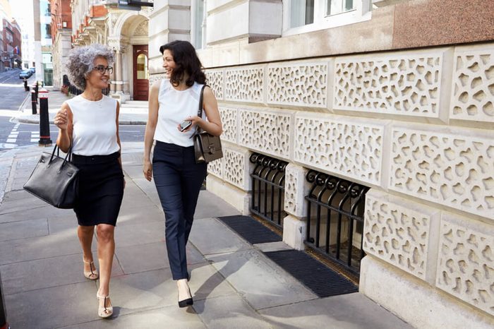 Two women walking in the street talking, full length