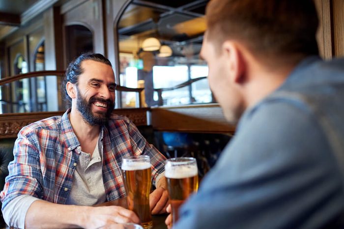 people, men, leisure, friendship and communication concept - happy male friends drinking draft beer at bar or pub