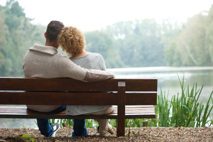 Rear view of a happy couple sitting together on bench outdoors