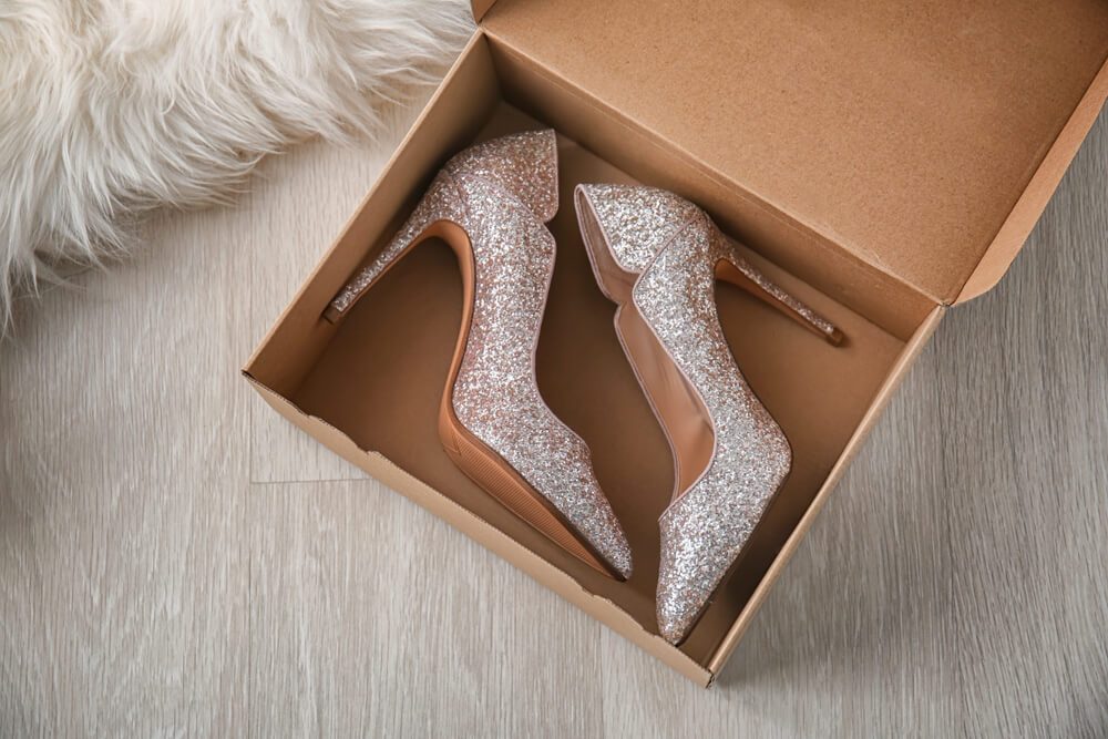 Box with pair of sparkly female shoes on floor, top view