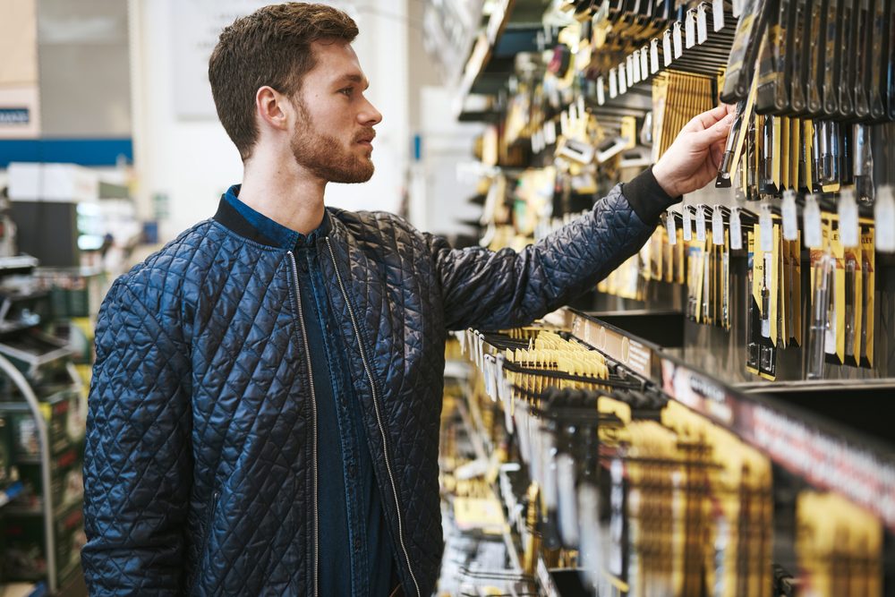 Bearded young man in a hardware store standing reading the information on a product hanging on the rack, side view close up