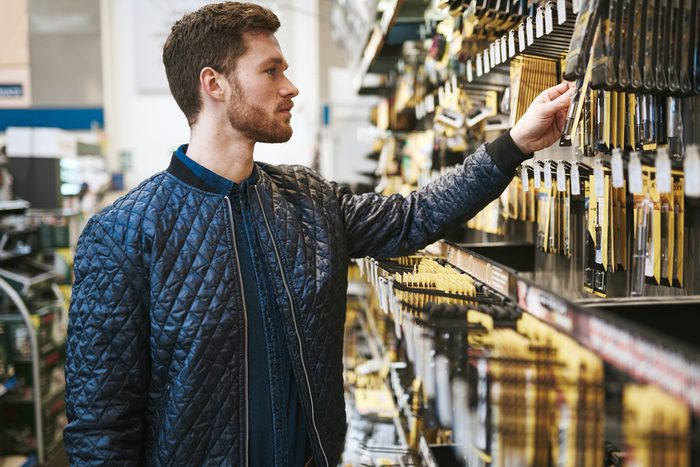 Bearded young man in a hardware store standing reading the information on a product hanging on the rack, side view close up