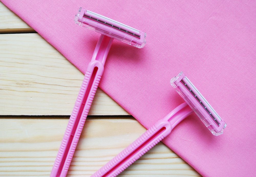 Couple of pink women's disposable razors on wooden table.