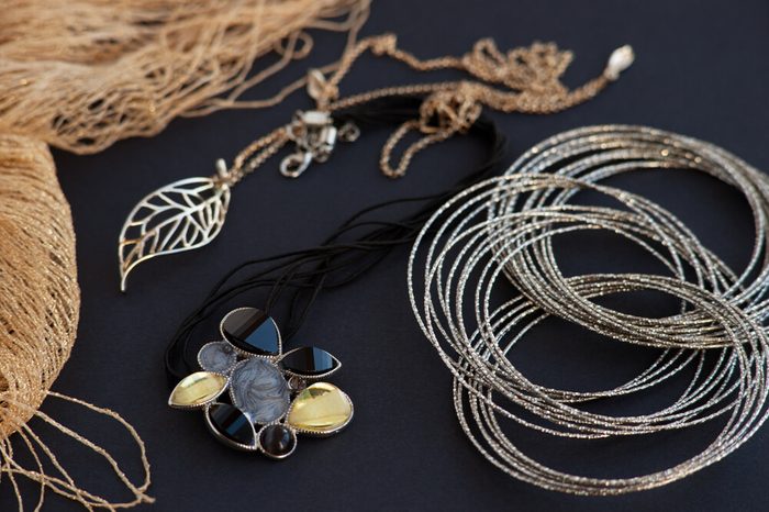 Jewelry on a black background. Golden scarf and chain on a black background. Bijouterie in golden tones on a black background looks luxurious. Silver bracelet . Style, fashion and design of jewelry.