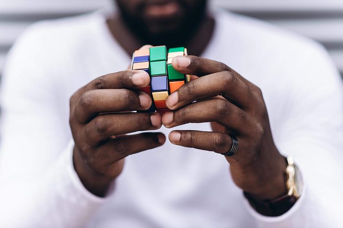 Kyiv, Ukraine - May 17th, 2017: Handsome Afro American man wearing casual clothes collect Rubik's Cube. Rubik's cube invented by a Hungarian architect Erno Rubik in 1974.