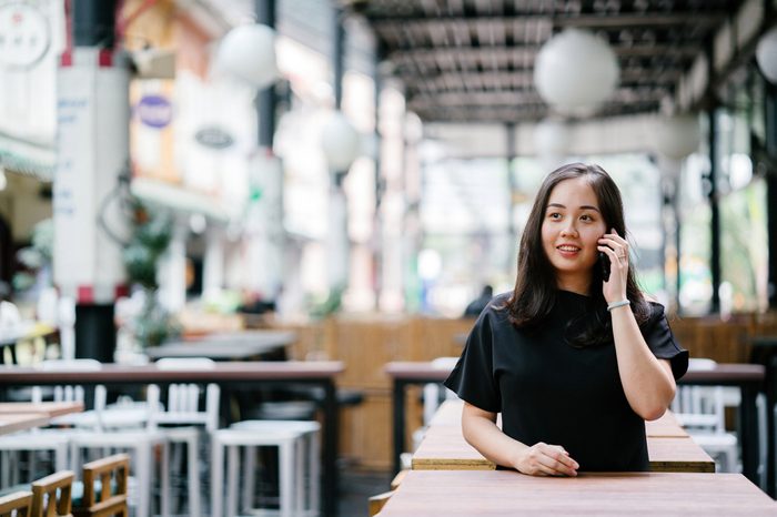 A young and attractive Chinese Asian woman is smiling while she's talking on her smartphone in a city in Singapore, Asia. 