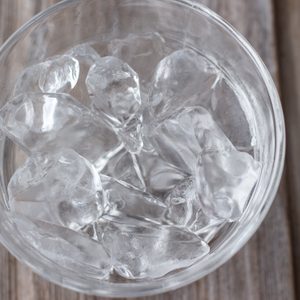 horizontal image of a clear glass bowl with ice cubes on a wooden background