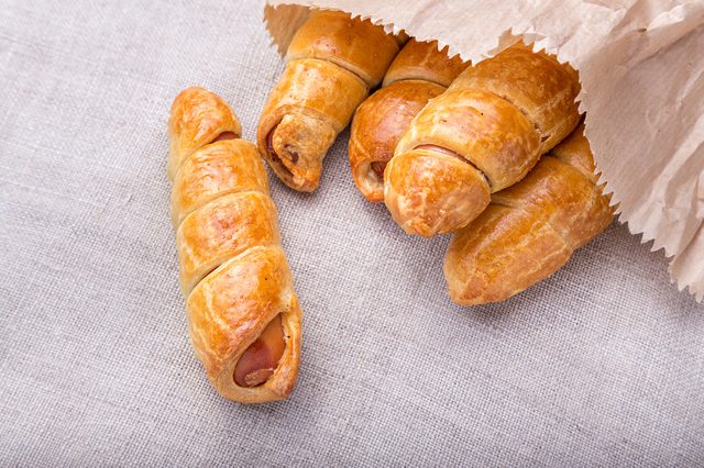 a plate of sausages in dough, homemade pastries, standing on a blue wooden surface. under the plate is a linen napkin. top view